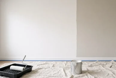 Half-painted living room wall with a roller tray, masking tape and drop sheets during a house repaint